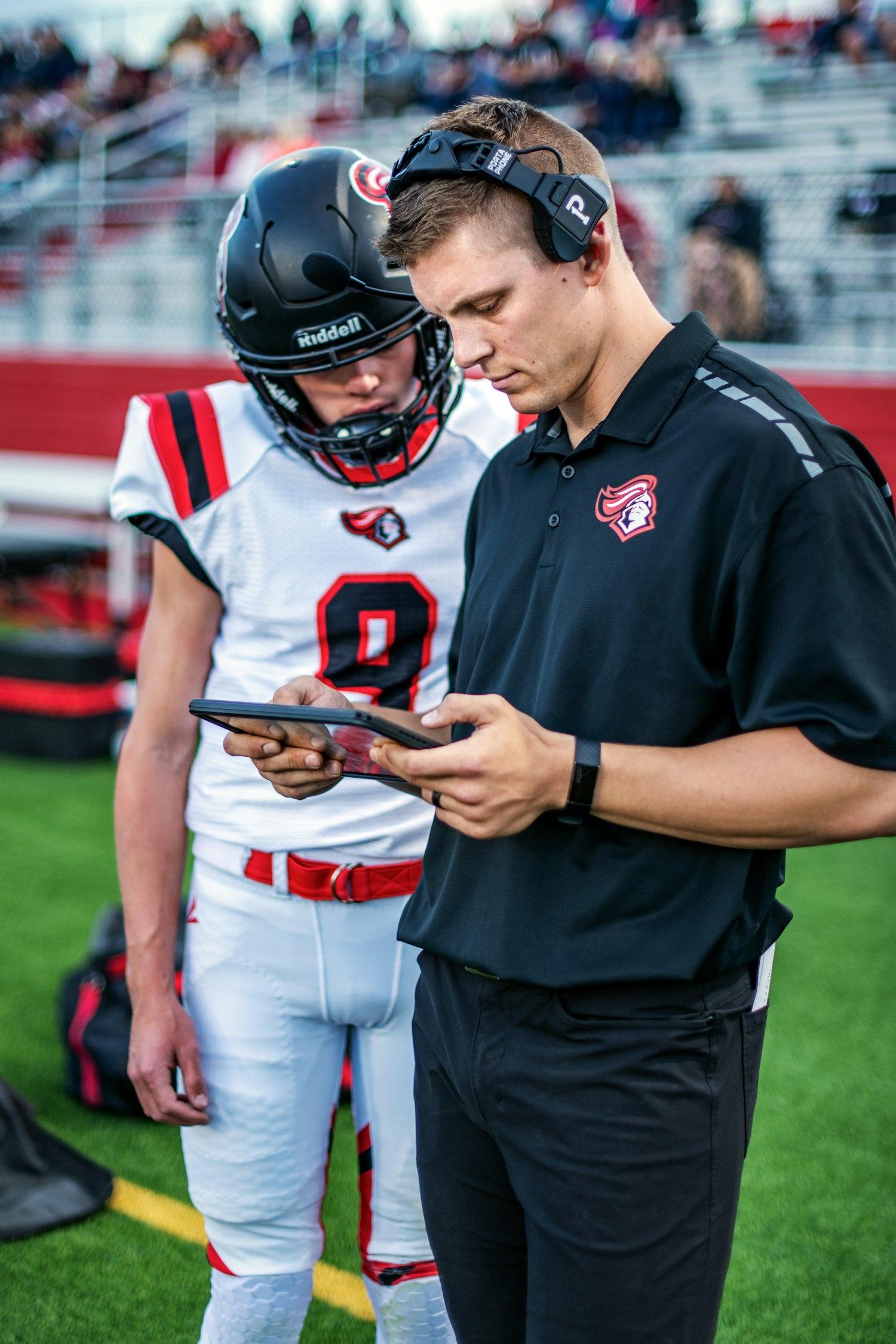 A coach and player reviewing stats on a tablet on the sideline
